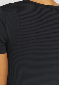 Mustapohjainen urheilupaita, jossa on tekstuuri ja ribbikuvio, lyhyet hihat ja sileä kaula-aukko mukavuutta ja joustavuutta varten.