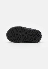 Suola di scarpa in gomma nera con modelli di presa testurizzati, creste e un distintivo dettaglio a linea curva al centro.
