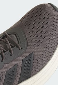 Sivé atletické topánky s sieťovinovým zvrškom, perforovanou textúrou a gumovými akcentmi. Majú hrubú bielu podrážku a kontrastné šnúrky.