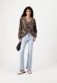 Sweater med leopardprint, V-hals og lange ærmer, parret med lyseblå udvidede jeans og beige ballerinaer. Sort håndtaske i hånden.