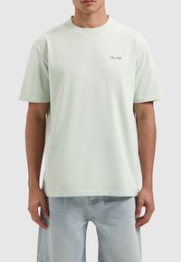 Lichtgroene katoenen t-shirt met korte mouwen, ronde hals en een klein geborduurd logo aan de linkerkant. Ontspannen pasvorm.