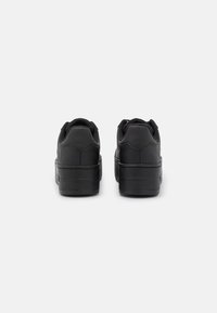 Un paio di sneakers nere con plateau viste da dietro su uno sfondo grigio chiaro semplice.