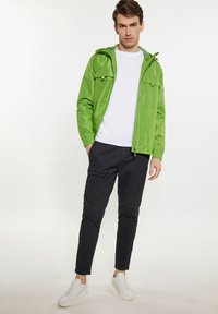 Grön, lättvikts zip-jacka med huva, elastiska muddar och två framfickor. Matchad med svarta byxor och vita sneakers.