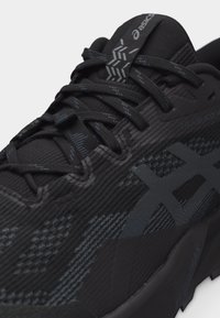 Κοντινή λήψη μαύρου παπουτσιού τρεξίματος Asics με πλεκτό άνω μέρος με σχέδιο, ανακλαστικό λογότυπο, ενισχυμένα κορδόνια και μαλακή σόλα για αθλητική χρήση.