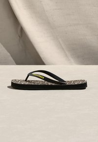 Μαύρο σαγιονάρι με ανατομικό πέλμα σε λεοπάρ σχέδιο και κίτρινο κείμενο «DSQUARED2» στο λουράκι, τοποθετημένο πάνω σε μπεζ υφασμάτινο φόντο.