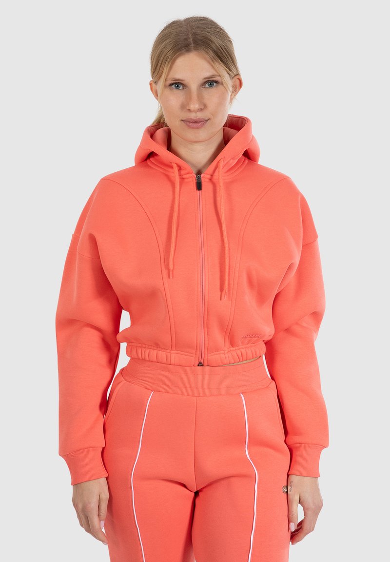 Felpa con zip corallo dal taglio rilassato, con vita elastica e due tasche frontali. Caratterizzata da un tessuto testurizzato e cappuccio con lacci.