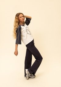 Wit en navy raglan mouwshirt met grafische print, gecombineerd met navy broek en grijze sportschoenen. Zachte stof, losse pasvorm, casual kleding.