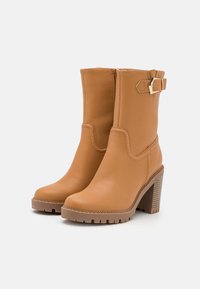 Botas de tobillo de cuero marrón con punta redonda, tacón grueso, detalle de hebilla y suela texturizada. Presentan una superficie lisa y costuras en la parte superior.