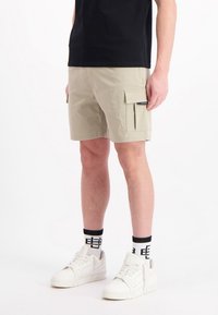 Lichtbeige cargo shorts met zijzakken, gemaakt van zacht materiaal. Gecombineerd met een zwart shirt en witte sneakers, met geprinte sokken.