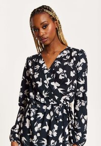 Black wrap dress with white floral pattern, long sleeves, v-neckline, and tie waist. Smooth fabric with slight sheen and gathered cuffs.