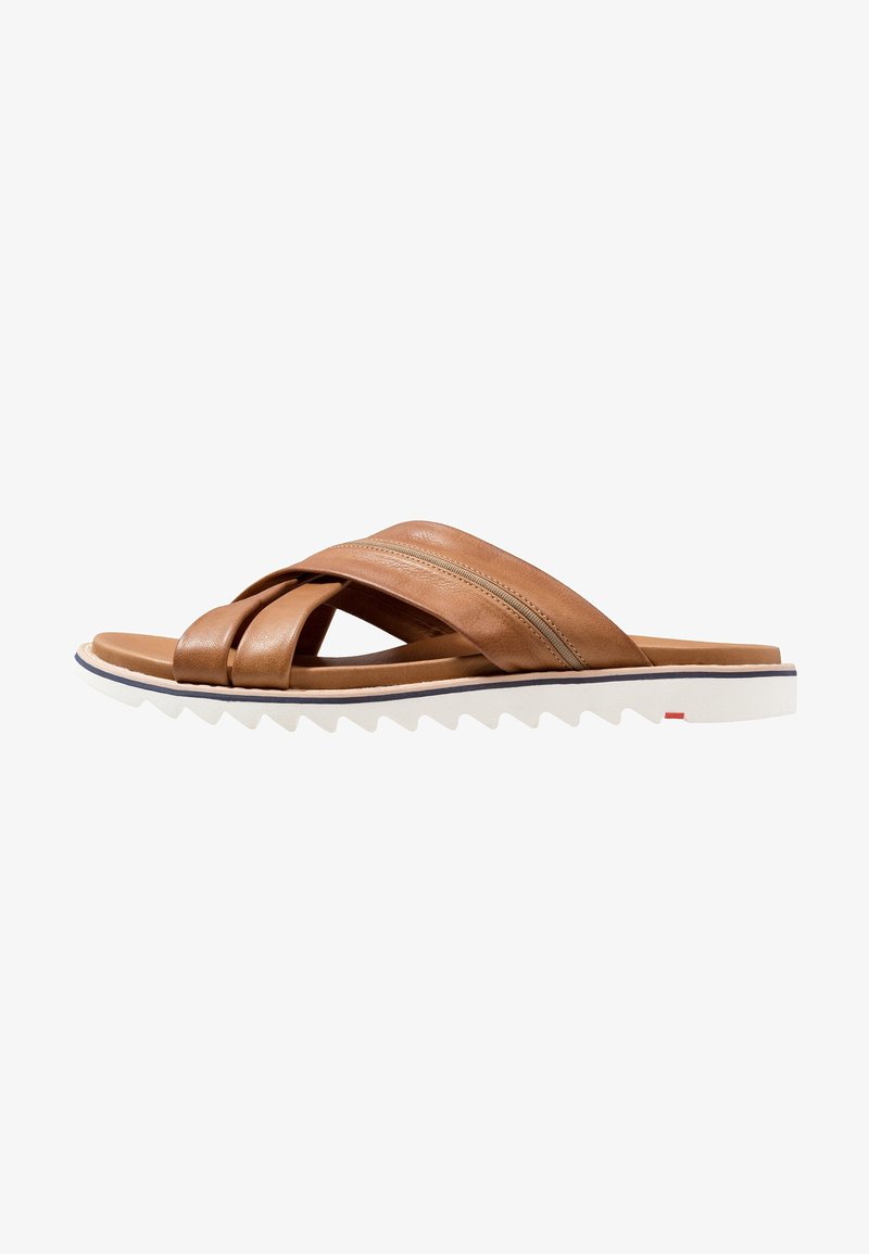 Sandale en cuir marron avec des lanières entrecroisées, semelle plate et semelle extérieure en caoutchouc blanc texturé avec des bords dentelés et un accent rouge.