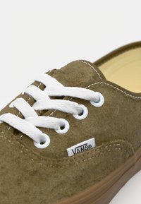 Bruine suède sneaker met witte veters, ronde oogjes en een logo patch. De buitenzool is beige en heeft een eenvoudig, klassiek ontwerp.