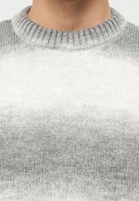 Λαιμός και άνω μέρος στήθους ατόμου που φοράει πουλόβερ πλεκτό σε γκρι και λευκή διαβάθμιση, με ριγωτό στρογγυλό γιακά.