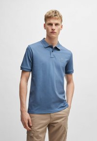 Niebieska koszulka polo z mieszanki bawełny, z klasycznym kołnierzykiem, zapinana na dwa guziki oraz z małą naszywką z logo na piersi.