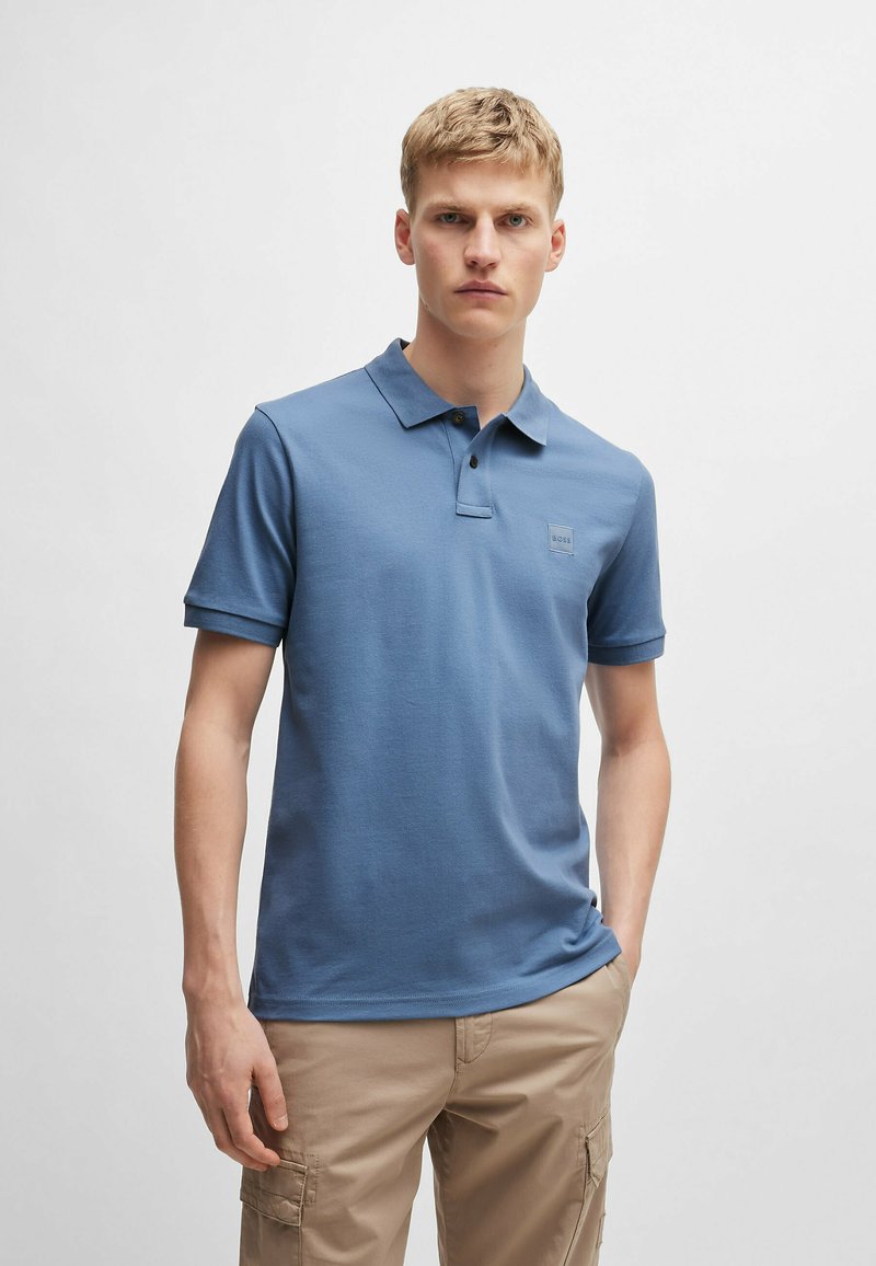 Niebieska koszulka polo z mieszanki bawełny, z klasycznym kołnierzykiem, zapinana na dwa guziki oraz z małą naszywką z logo na piersi.