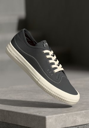 Dark gray sneaker with textured leather upper, cream laces, and rubber sole featuring vertical ridges. Minimalist design and stitching details.