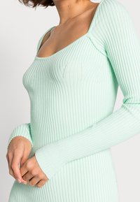Vestido de manga larga acanalado en verde menta. Presenta un escote cuadrado y un diseño ajustado con detalles de texturas. Las mangas tienen bordes en forma de concha.