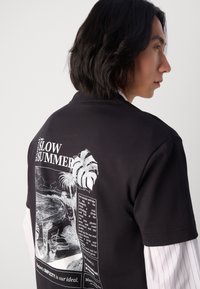 Black cotton t-shirt featuring white graphic print on the back, showcasing palm trees and text, round neckline, and short sleeves.