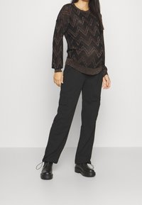 Maglione nero a maniche lunghe con un motivo a zigzag in fili metallici, abbinato a pantaloni cargo neri e stivali neri chunky.