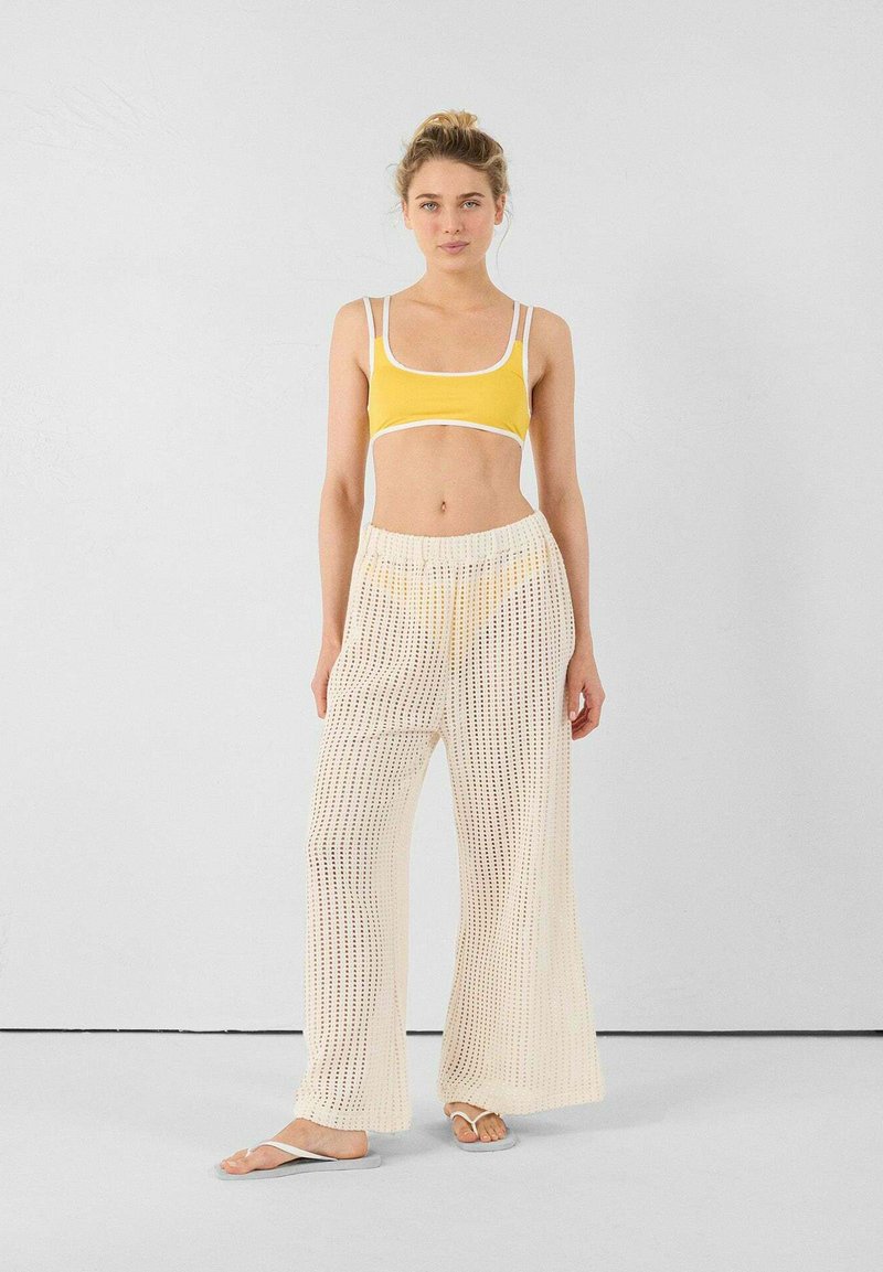 Reggiseno sportivo giallo con dettagli bianchi, abbinato a pantaloni allentati color crema in crocheted con una texture a motivi. Infradito coordinate.