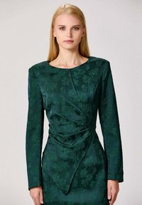 Robe longue à manches longues avec un motif floral vert, col rond et détail drapé à l'avant. Tissu lisse avec un léger éclat et épaules structurées.