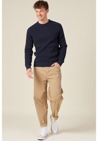 Maglione lavorato a maglia blu navy con scollatura rotonda, abbinato a pantaloni khaki e sneaker bianche per un look casual. Texture liscia in tutto il capo.