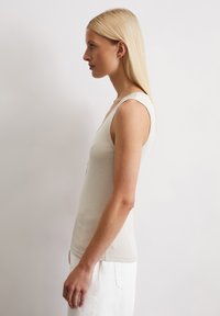 Aansluitend, mouwloos tanktop in lichtbeige ribbelstof, met een V-hals en een soepele textuur, gecombineerd met witte denim shorts.