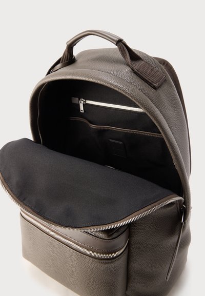 Καφέ δερμάτινο σακίδιο με υφή, με ανοιχτό κύριο διαμέρισμα που δείχνει μαύρο εσωτερικό, τσέπη με φερμουάρ, μπροστινή θήκη με φερμουάρ και μαλακή λαβή στην κορυφή.