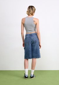Top cropped gris y pantalones cortos de cargo de mezclilla azul, con dos bolsillos traseros, corte relajado y un diseño hasta la rodilla. Zapatos negros y azules.