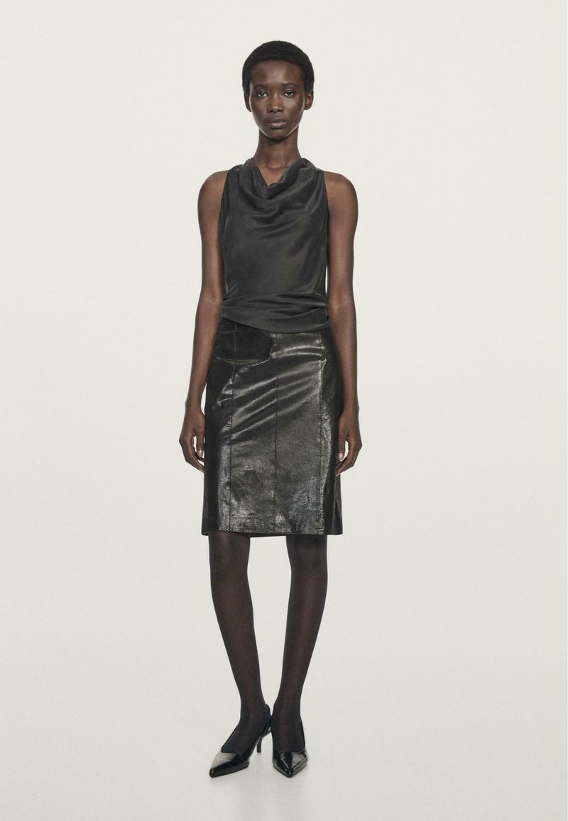 Haut en satin noir à col bénitier associé à une jupe crayon en cuir noir. Le modèle porte des collants noirs et des escarpins à bout pointu. Texture lisse, design épuré.