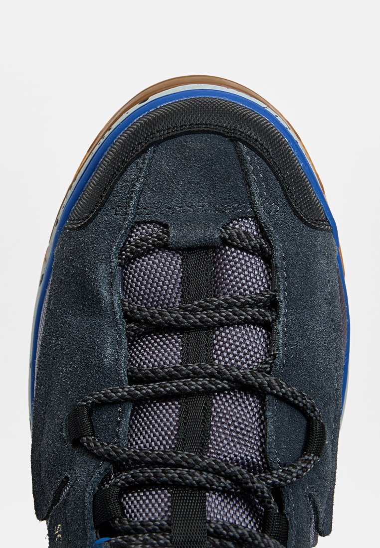 Dunkelblaue Wildleder-Sneaker mit einem strukturierten Mesh-Obermaterial. Schwarze Schnürsenkel und eine mehrfarbige Gummisohle. Sichtbare Nähte und gepolsterte Kanten.