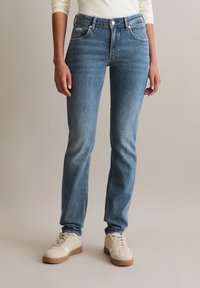 Jasnoniebieskie dżinsy z wysokim stanem, prostą nogawką, delikatnymi zmechaceniami oraz klasycznym pięciopocketowym stylem, zestawione z beżowymi tenisówkami.