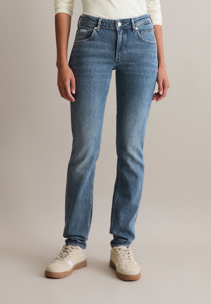 Jasnoniebieskie dżinsy z wysokim stanem, prostą nogawką, delikatnymi zmechaceniami oraz klasycznym pięciopocketowym stylem, zestawione z beżowymi tenisówkami.