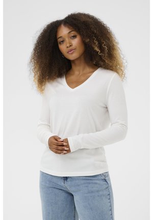 Weißes langärmliges V-Ausschnitt-Oberteil aus weichem Material, mit lässigem Schnitt und betonten Bündchen. Kombiniert mit hellblauen Denim-Jeans.