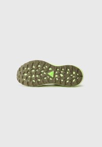 Semelle de chaussure de sport présentant une surface en caoutchouc brun texturé avec des motifs de semelle triangulaires et circulaires, soulignée par un bord vert néon.