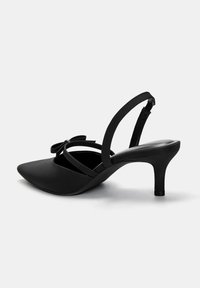 Svart högklackad slingback-sko med spetsig tå, dekorerad med en rosett och tunna remmar. Slät yta med en elegant design.