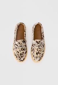 Une paire de chaussures slip-on avec un motif de taches beige et marron foncé et des semelles en cuir sur un fond blanc.