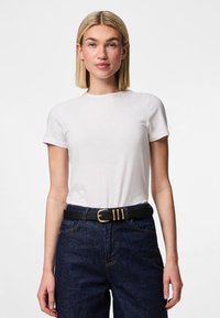 T-shirt branca de manga curta feita de algodão, combinada com jeans de ganga azul-escuro e um cinto preto com fivela dourada.