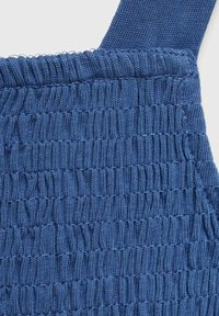 Gros plan sur un tissu tricoté bleu avec un smocking élastique et une sangle, mettant en valeur la texture côtelée et froncée détaillée.