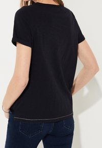 Sort T-shirt med korte ærmer og opfoldede kanter, rund udskæring, blød tekstur og lige underkant med en kontrastsyet detalje.