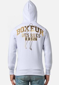 Felpa bianca con scritta dorata sulla schiena che recita "BOXEUR DES RUES." Presenta un cappuccio con coulisse e polsini a coste.