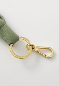 Cintura in pelle verde con hardware in metallo dorato, caratterizzata da un anello circolare e un gancio a scatto. Texture liscia con dettaglio del marchio.