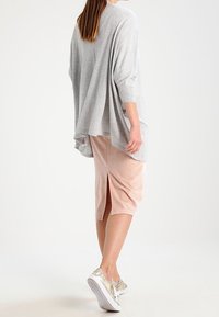 Lätt, grå, oversized topp med 3/4 ärmar; kombinerad med en ljusrosa kjol i knälängd med sidoslitsar; guld sneakers.