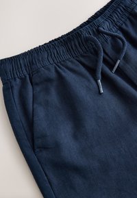 Close-up of navy blue sweatpants waistband with elastic band and drawstring ties on a light background.