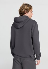 Felpa grigia scura con vestibilità comoda, dotata di un ampio cappuccio, polsini a coste e cuciture laterali. Texture morbida, design minimale.