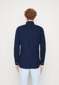 Tmavě modrá košile s malým geometrickým vzorem, dlouhými rukávy, přiléhavého střihu, límečkem na knoflíky a manžetami na knoflíky.