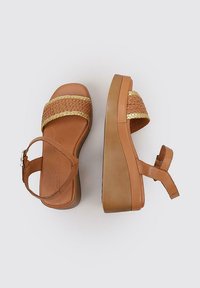 Brown wedge sandals featuring woven straw straps, a smooth synthetic sole, and an adjustable ankle strap. Textured upper with a subtle sheen.