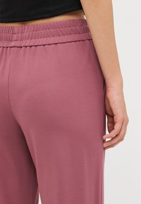 Roze elastische broek van stof met een elastische tailleband. Glad oppervlak, comfortabele pasvorm, met een zijnaaddetail vlak boven de zoom.