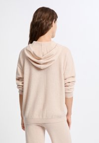 Felpa cappuccio color beige chiaro con texture morbida, caratterizzata da una vestibilità comoda, polsini a coste e cappuccio a doppio strato.