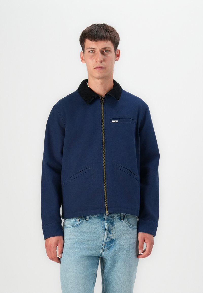 Chaqueta azul marina con un cuello de pana negro, cremallera frontal y bolsillo en el pecho; fabricada con un tejido resistente; cuenta con dos bolsillos laterales.